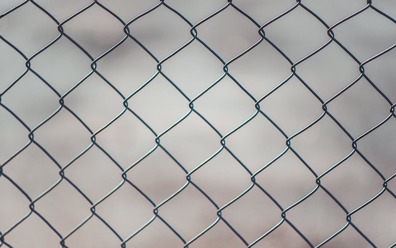 Detailed closeup of a metal chain-link fence with a blurred neutral background, perfect for textures and overlays.